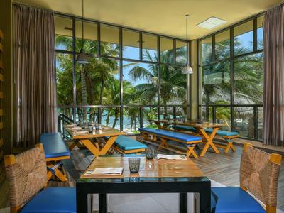 Vista di una moderna zona ristorante dell'hotel con tavoli in legno, cuscini blu e grandi finestre con vista sulle palme.