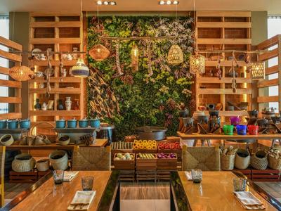 Ristorante moderno con parete verde di piante, arredi in legno caldo e decorazioni colorate sui tavoli