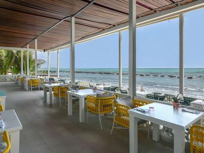 Area ristorante moderna sulla spiaggia con tavoli bianchi e sedie gialle con vista sul mare