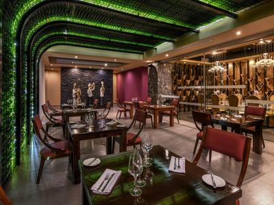 Ristorante moderno con legno scuro, illuminazione verde a parete e tavoli elegantemente apparecchiati.