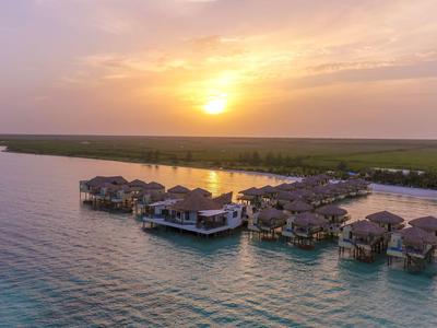 Západ slunce nad resortem s bungalovy na vodě v tropické laguně.