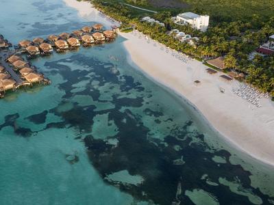 Letecký pohled na plážový resort s bungalovy nad vodou a čistým modrým mořem.