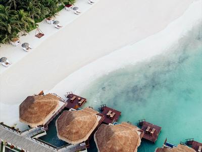 Letecký pohled na doškové chaty nad tyrkysovým mořem u bílé písečné pláže.