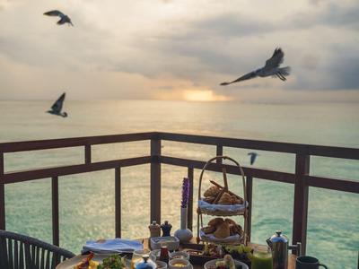 Stůl prostřený jídlem a pitím na terase s výhledem na moře při západu slunce.