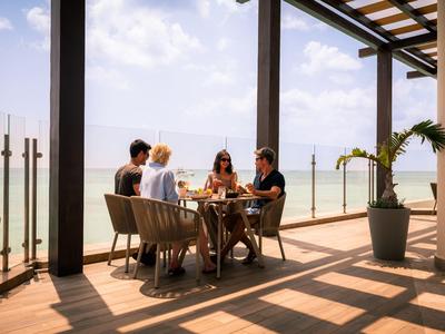 Čtyři lidé sedí u stolu na slunné terase s výhledem na moře.