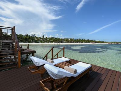 Dvě lehátka na dřevěné terase s výhledem na čistou mořskou vodu a částečně zataženou oblohu.