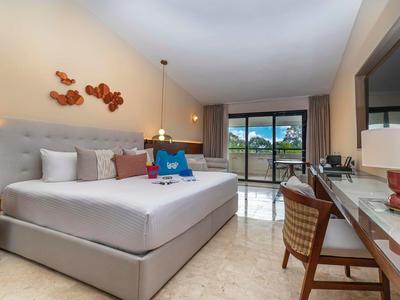 Hell eingerichtetes Hotelzimmer mit großem Bett, Schreibtisch, Stuhl und Balkon mit Meerblick.