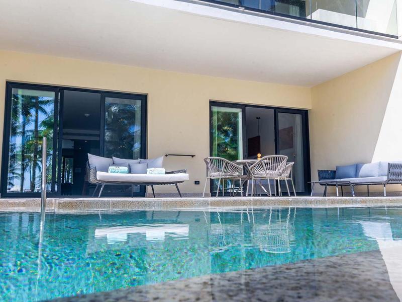 Area esterna moderna con piscina, divani e tavolo da pranzo davanti a un edificio con grandi finestre.