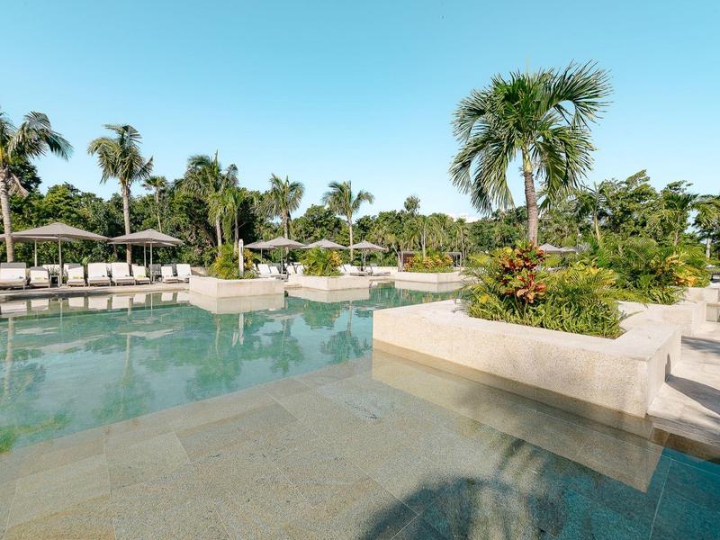 Ampia area piscina con palme e ombrelloni in una giornata soleggiata.