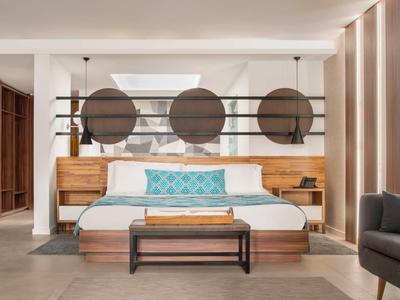 Moderní hotelový pokoj s velkou postelí, dekorativními polštáři a stylovými dřevěnými prvky.