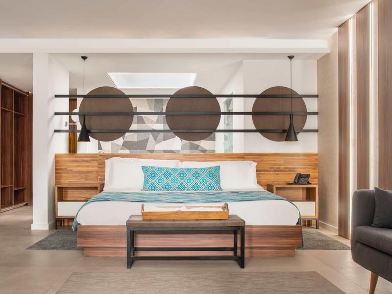 Moderní hotelový pokoj s velkou postelí, dekorativními polštáři a stylovými dřevěnými prvky.