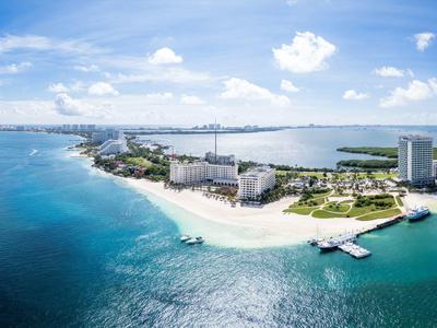 Spiaggia e hotel su una costa con acqua blu chiara e cielo parzialmente nuvoloso.