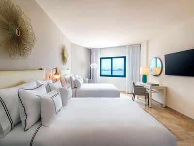 Camera d'hotel moderna con due letti matrimoniali, TV e finestra con vista esterna.