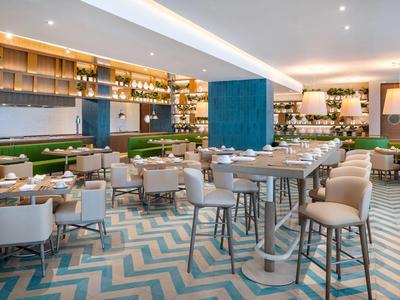 Modernes Restaurant mit hellen Stühlen, grünem Sofa, hölzernen Regalen und Zickzack-Musterboden.