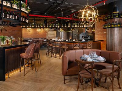 Bar d'hotel elegante con sgabelli, tavoli rotondi e decorazioni in legno caldo sotto una luce sferica dorata.