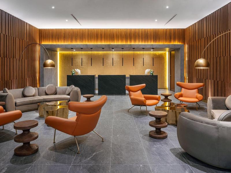 Lounge d'hotel moderna con divani grigi, poltrone arancioni e pannelli in legno.