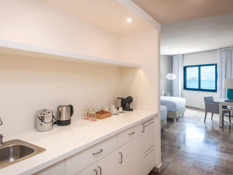 Camera d'hotel moderna con angolo cottura, scrivania e grande finestra.