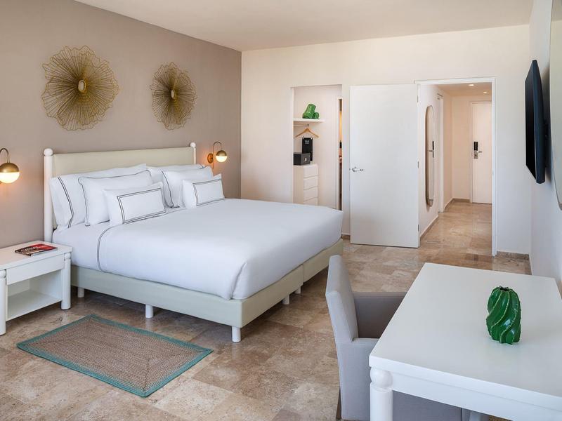 Camera d'hotel moderna con letto grande, scrivania e arredi chiari e accattivanti.