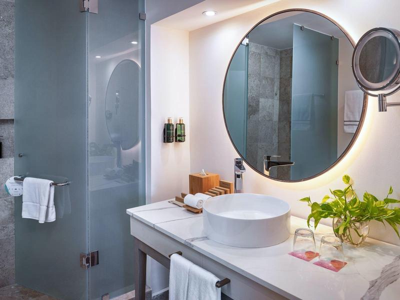 Bagno moderno con specchio rotondo, lavabo e doccia in vetro.