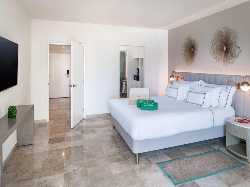 Camera d'hotel luminosa con grande letto matrimoniale, TV a parete e arredi moderni.