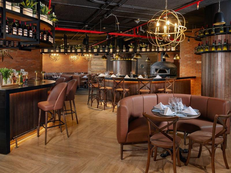 Bar d'hotel elegante con sgabelli, tavoli rotondi e decorazioni in legno caldo sotto una luce sferica dorata.