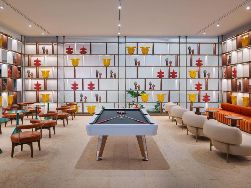 Area lounge moderna con tavolo da biliardo, poltrone eleganti e scaffali decorativi a parete.