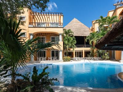 Hotel con piscina rodeada de palmeras y vegetación tropical bajo un cielo azul.