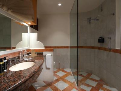 Baño moderno con lavabo de granito, ducha de vidrio y azulejos con patrón.