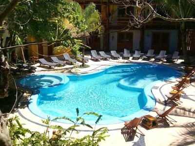 Ein rundlicher Pool mit Liegestühlen und Bäumen im Schatten eines Hotels.