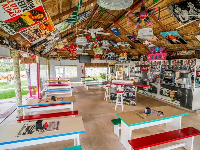 Restaurant ouvert décoré coloré avec toit en bois rustique et bancs colorés.