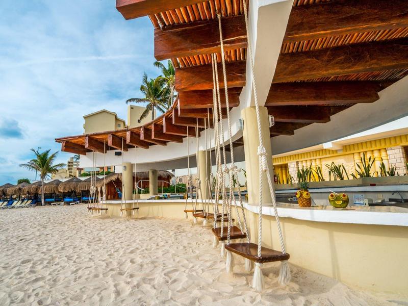 Plage de sable avec balançoires suspendues sous un espace couvert dans un hôtel tropical