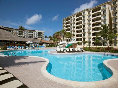 Gran piscina del resort con tumbonas y edificios de varios pisos al fondo bajo un cielo azul.
