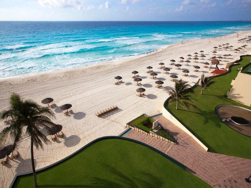 Plaża z parasolami, palmami i zadbaną trawą obok morza.