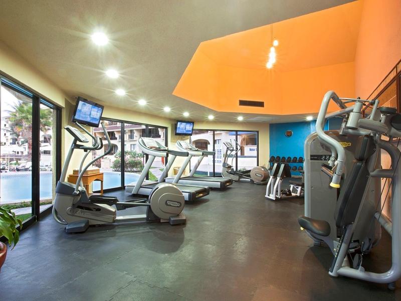 Jasna siłownia z bieżniami, sprzętem treningowym i pomarańczowym sufitem w hotelu.