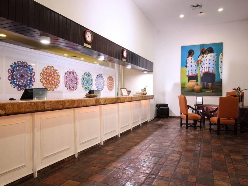 Réception d'hôtel moderne avec long comptoir, décor en verre coloré et coin salon adjacent.