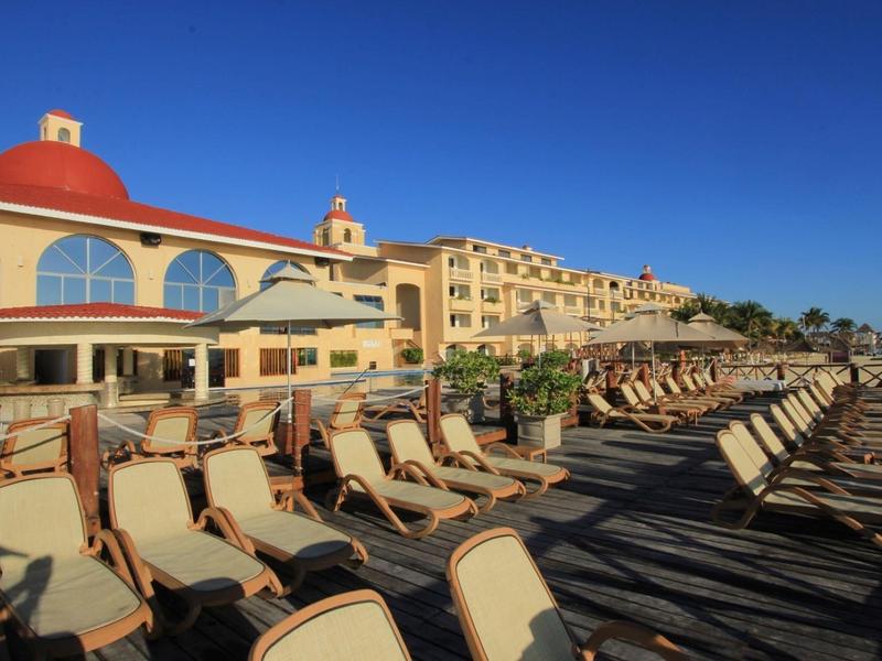 Terrasse d'hôtel ensoleillée avec de nombreuses chaises longues sous un ciel bleu clair.