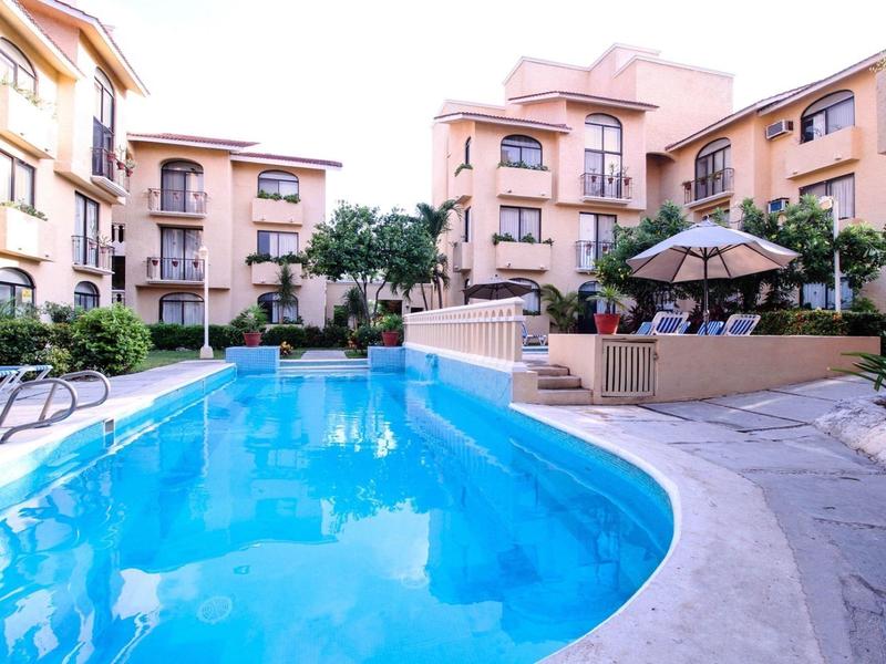Piscine d'hôtel entourée de bâtiments à plusieurs étages et de palmiers sous un ciel clair.