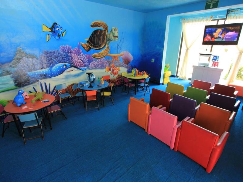 Salle de jeux pour enfants colorée avec fresque murale sous-marine, petites tables et chaises, et rangées de sièges.