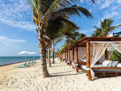 Sandstrand mit Palmen, Sonnenliegen und Holzpavillons mit weißen Vorhängen unter blauem Himmel.