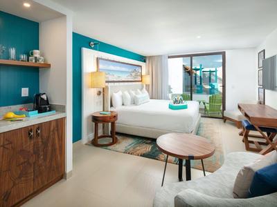 Camera d'hotel moderna con letto, zona soggiorno, TV e balcone con vista mare.