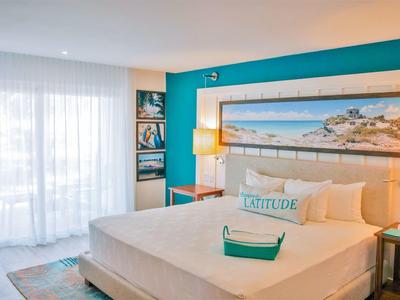 Camera d'hotel luminosa con grande letto, lenzuola bianche lisce e dipinto marino sulla parete.