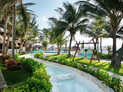 Area tropicale dell'hotel con piscina, sedie sospese e palme sotto un cielo limpido.
