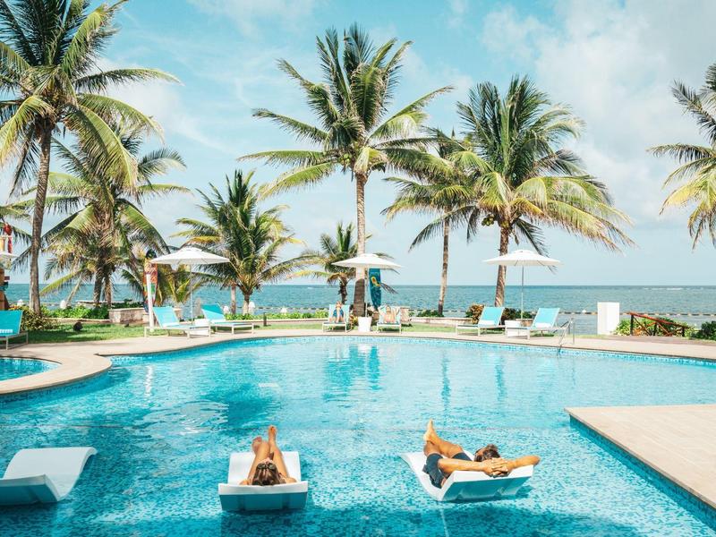 Zona piscina rilassante con lettini in acqua e palme vicino al mare