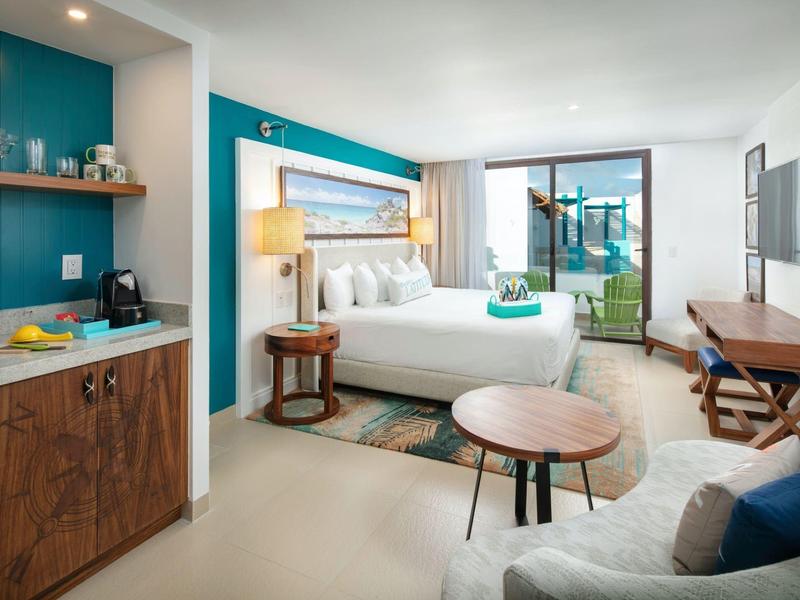 Camera d'hotel moderna con letto, zona soggiorno, TV e balcone con vista mare.