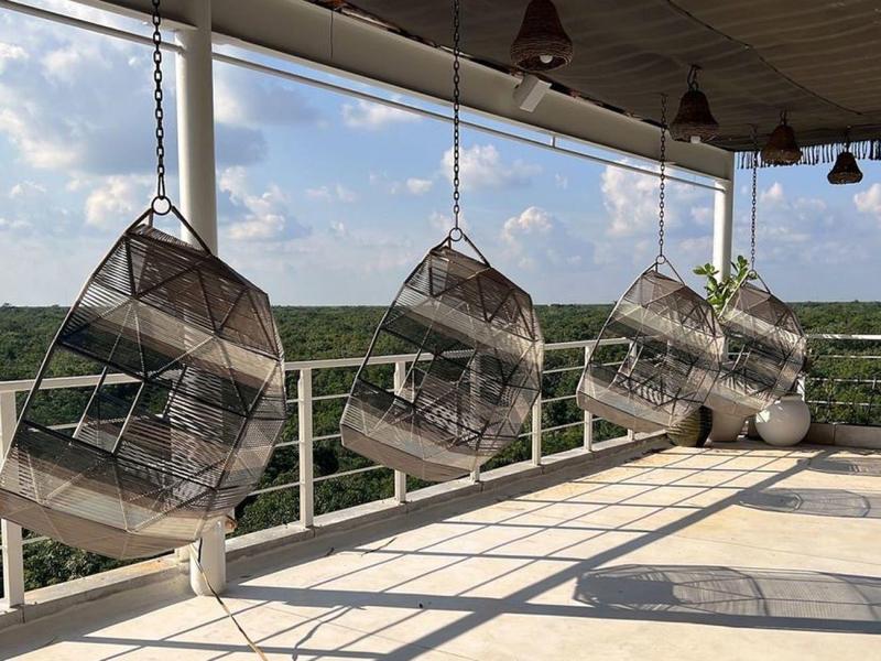 Zadaszony taras z czterema wiszącymi krzesłami z rattanu z widokiem na zielony krajobraz.