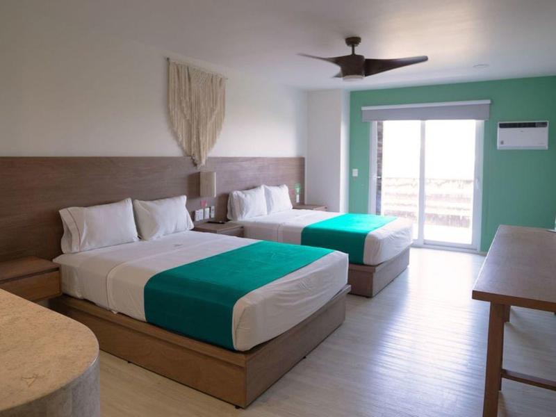 Nowoczesny pokój hotelowy z dwoma łóżkami podwójnymi, zieloną ścianą akcentową i balkonem z widokiem na morze.