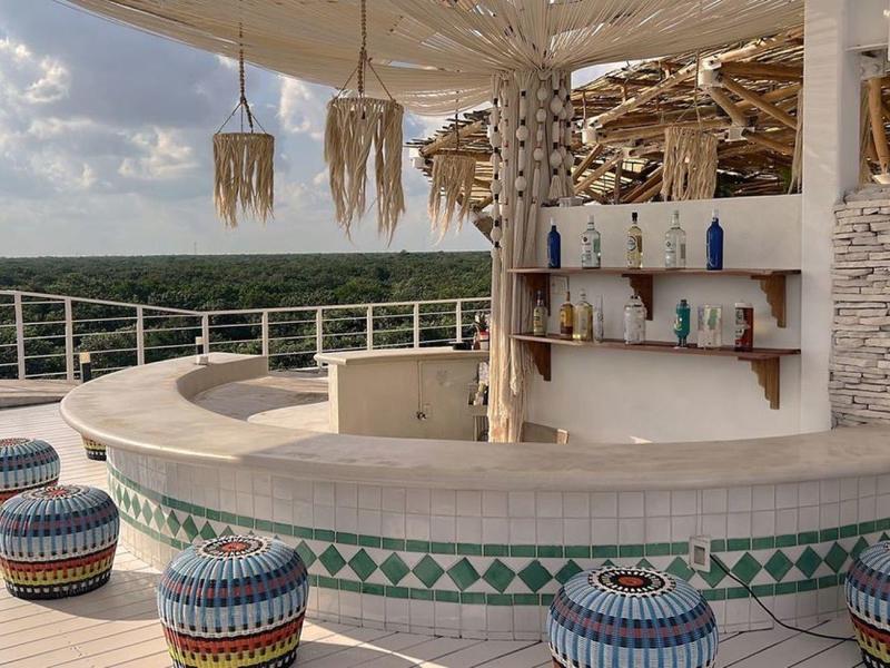 Zewnętrzny bar hotelowy z okrągłymi stołkami i ozdobnymi trójkątnymi płytkami pod niebieskim niebem.