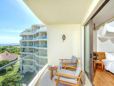 Balkon met stoelen en zeezicht vanuit een hotelkamer met open slaapkamer.