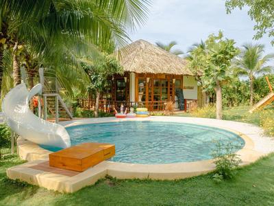 Rond zwembad met glijbaan en houten hut omgeven door tropische planten.