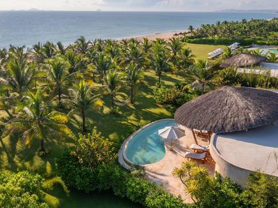 Luxe strandvilla met zwembad, omgeven door palmbomen en uitzicht op zee.